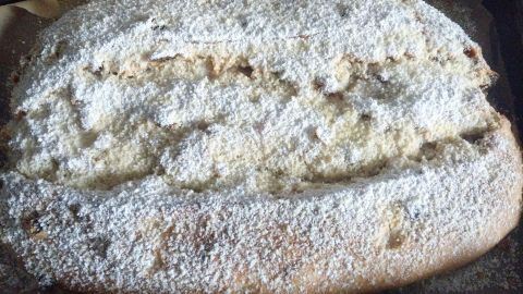 Ein frisch gebackener Butter-Rosinen-Stollen liegt auf einer Backplatte, bestäubt mit Puderzucker und umgeben von Backpapier.
