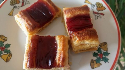 Kleine, gebräunte Gebäcke mit roter Marmelade auf einem festlichen Teller, umgeben von weihnachtlichen Motiven.