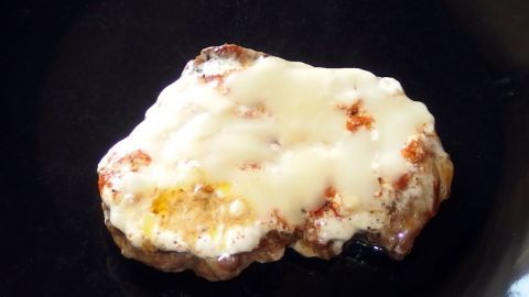 Ein überbackenes Schnitzel liegt auf einem schwarzen Teller, überzogen mit geschmolzenem Käse und goldbraunen Rändern.