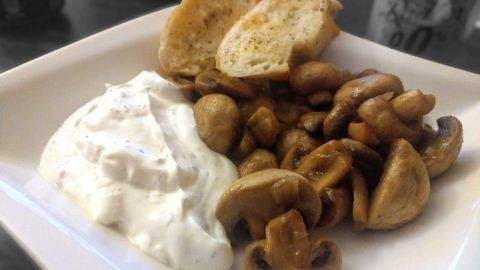 Saftige Champignons liegen auf einem Teller, neben einer cremigen Sauce und frischem Brot, bereit zum Genießen.