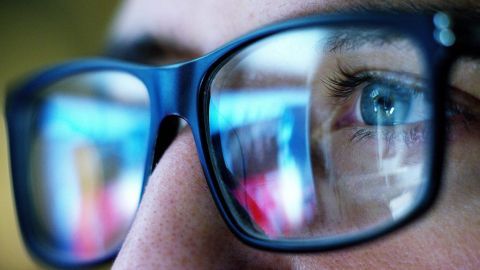 Eine Blaulichtfilter-Brille schmiegt sich um die Augen, während der Träger konzentriert auf einen PC-Bildschirm blickt.