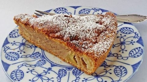 Ein Stück Apfel-Bananen-Kuchen ohne Zucker, verziert mit Puderzucker, liegt auf einem dekorativen Teller aus Porzellan.