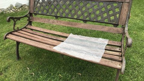 Auf einer Holzbank im Garten liegt Luftpolsterfolie als Sitzunterlage, um den Komfort im Freien zu erhöhen.
