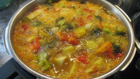 Ein großer Topf mit buntem Gemüseeintopf köchelt auf dem Herd, gefüllt mit gesunden Zutaten wie Brokkoli und Paprika.