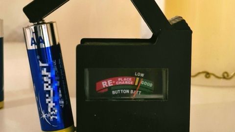 Ein Batterieprüfer überprüft eine AA-Batterie in der Nähe einer LED-Kerze und zeigt den Ladezustand an.