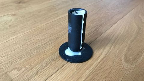 Eine schwarze Kerze steht auf einem Parkettboden, umgeben von flüssigem Kerzenwachs, das nach unten tropft.
