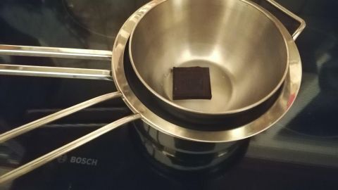 Eine Edelstahlschüssel mit einem Stück Schokolade steht auf einem Wasserbad, um die Schokolade sanft zu schmelzen.