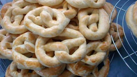 Eine große Menge goldbrauner, butterreicher Neujahrsbrezeln liegt übereinander auf einem silbernen Gitter.