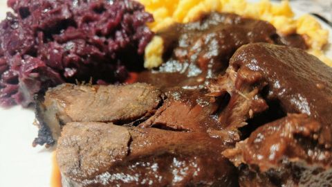 Saftige Rehkeule in Holundersoße auf einem Teller, begleitet von Rotkraut und einem cremigen Kartoffelbrei.