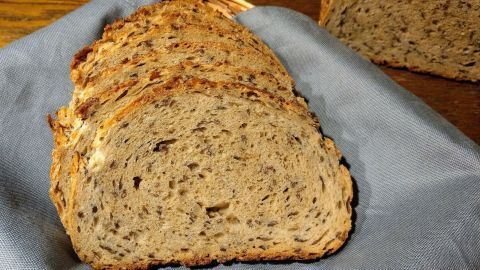 Ein frisch geschnittenes Dinkelbrot mit verschiedenen Körnern liegt auf einem blauen Tuch, bereit zum Servieren.