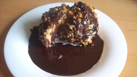 Eine Eispraline liegt auf einem weißen Teller, überzogen mit reichhaltiger Nugat-Soße und gehackten Nüssen.