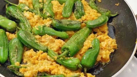 Bratpaprika liegt gebraten auf einer Pfanne mit goldbrauner Textur, umgeben von einem aromatischen, schaumigen Gericht.