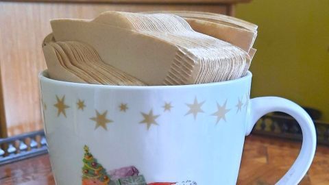 Eine weihnachtliche Tasse hält Filtertüten, umgeben von einem hölzernen Tisch und einer festlichen Atmosphäre.