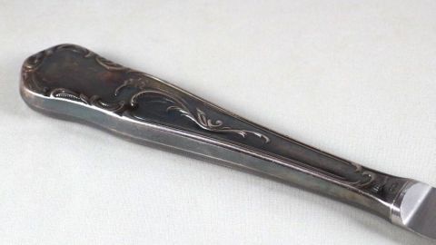 Mit Zigarettenasche kann man sehr gut Silber reinigen. Ein silberner Löffel liegt auf einer hellen Oberfläche und wird mit Zigarettenasche gereinigt, um seinen Glanz wiederherzustellen.