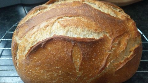 Ein rustikaler Brotlaib mit knuspriger Kruste liegt auf einem Gitter, um abzukühlen, in einer gemütlichen Küche.