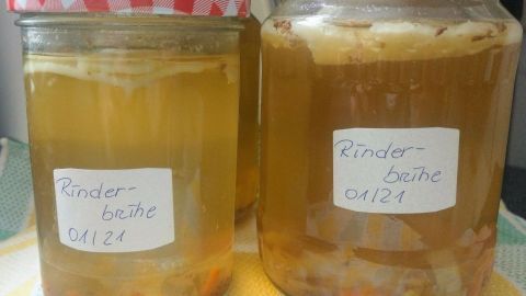 Zwei Gläser mit Rinderbrühe stehen auf einem bunten Tuch, gefüllt mit klarer Brühe und gemischtem Gemüse.