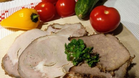 Auf einem Holzbrett liegt zarter Rinderbraten, garniert mit Petersilie, umgeben von frischem Gemüse wie Tomaten und Gurke.