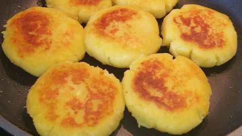 Goldene Kartoffelküchle braten in einer Pfanne, wobei ihr Außenrand knusprig und die Oberseite leicht gebräunt ist.