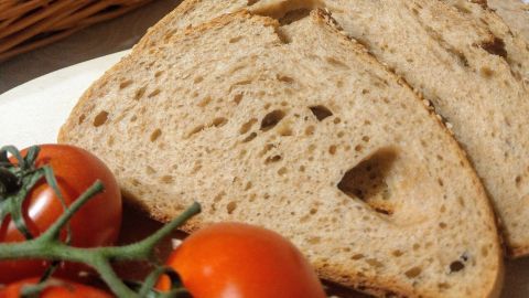 Schnitzel aus Vollkornbrot liegt neben Joghurt und frischen Tomaten auf einem Holzbrett in einer rustikalen Küche.