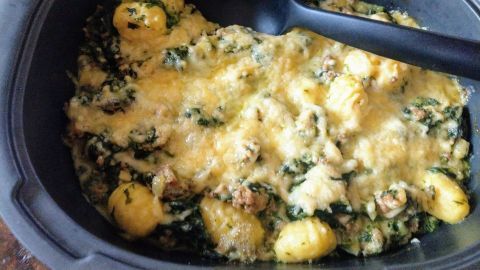 Ein cremiger Gnocchi-Spinat-Auflauf mit Gorgonzola ist in einer schwarzen Auflaufform zu sehen, serviert mit einem großen Löffel.