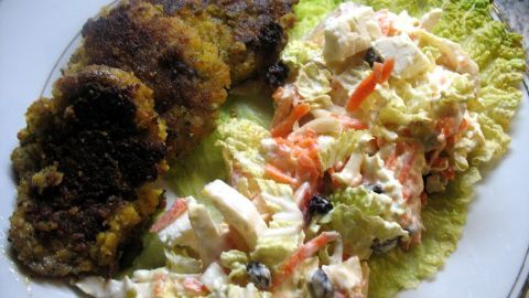 Kichererbsen-Bratlinge liegen knusprig auf einem Bett aus frischem grünen Salat, neben einem bunten Rahmsalat.
