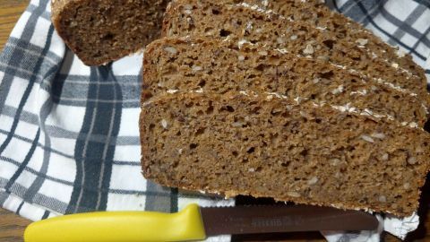 Ein frisch geschnittenes Dinkelvollkornbrot mit Körnern liegt auf einem karierten Tuch, umgeben von einem Holztisch.