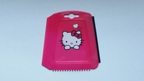 Ein rosa Eisschaber mit einem Hello-Kitty-Motiv liegt auf einem weißen Hintergrund, bereit zum Schneiden oder Schaben.