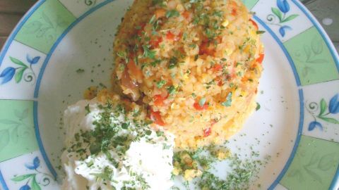 Ein schmackhafter Haufen Gemüse-Bulgur-Hanfsamen-Pfanne mit einer Portion cremigem Joghurt auf einem dekorativen Teller.
