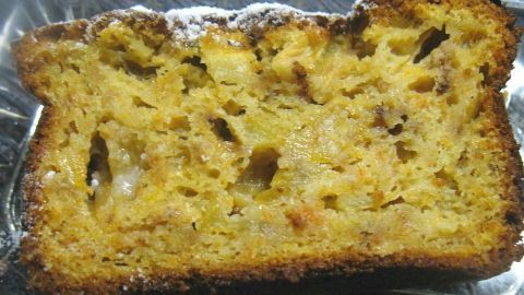 Ein saftiger Rührkuchen mit Apfel und Karotte liegt auf einem silbernen Teller, leicht mit Puderzucker bestäubt.