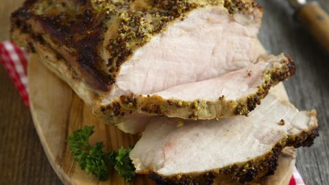 Ein saftiger Schweinebraten liegt auf einem Holzbrett, perfekt gegart, umgeben von einem karierten Tuch.
