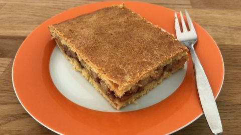 Ein Stück vegane, zuckerfreie Apfelschnitte liegt auf einem weißen Teller mit orangefarbenem Rand, daneben eine Gabel.