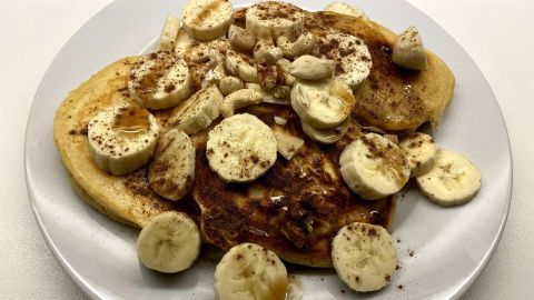 Auf einem weißen Teller liegen amerikanische Buttermilch-Pancakes, garniert mit Bananenscheiben und Zimt.
