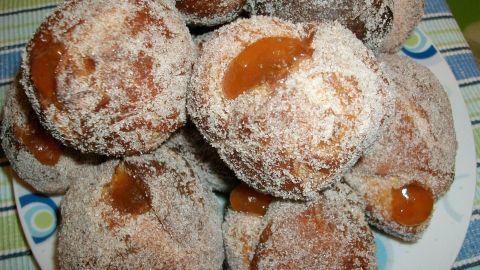 Puderzucker-bedeckte Mini-Berliner mit Marmelade obenauf sind in einem Teller auf einem bunten Tisch dargestellt.