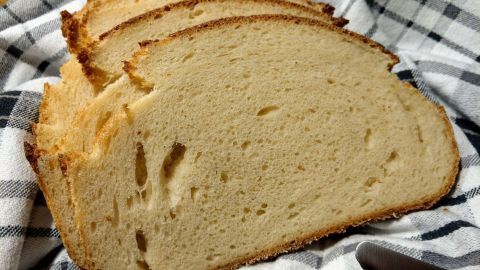 Scheiben eines Buttermilch-Dinkelbrots liegen auf einem karierten Tuch, umgeben von einem rustikalen Tisch.