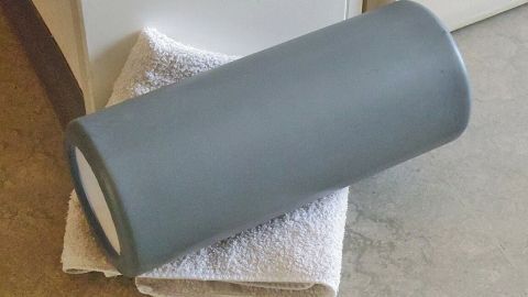 Ein grauer Faszienroller liegt auf einem weißen Handtuch und ist bereit für das Faszientraining im Innenraum.