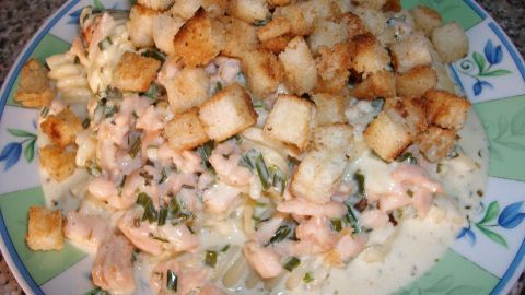 Fusilli in einer cremigen Lachs-Sahne-Soße wird von knusprigen Butter-Croutons begleitet und serviert auf einem bunten Teller.