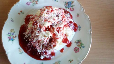 Zwei Teller Spaghetti-Eis stehen auf einem holzernen Tisch, die mit roter Soße und Kokosraspel dekoriert sind.