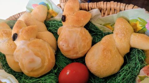In einem Korb liegen mehrere gebackene Osterhäschen aus Quark-Öl-Teig, umgeben von grünem Heu und einem roten Ei.