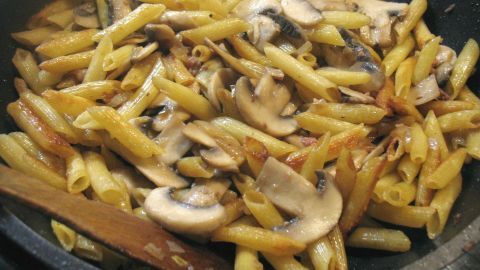 In einer Pfanne liegen goldbraun gebratene Nudeln mit Champignons, vermischt in einer cremigen Sauce.