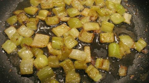 Karamellisierter Staudensellerie brät in einer Pfanne, während die Stücke in Butter leicht bräunen und glänzen.