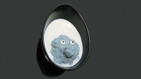 Ein blau gefärbter Milchreis mit Zuckeraugen sitzt in einer schwarzen Schale, umgeben von milchiger Flüssigkeit.