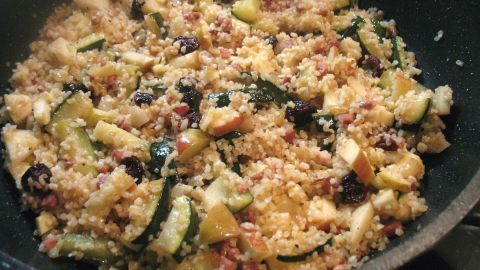 In einer Pfanne wird eine bunte Mischung aus Zucchini, Bulgur, Äpfeln und Rosinen zubereitet.