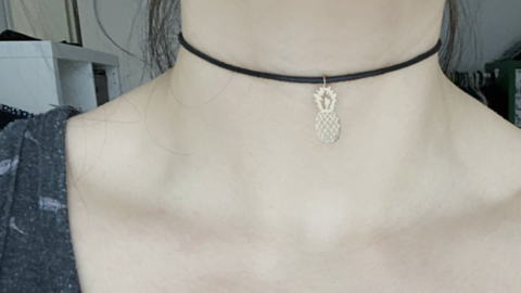 Ein Choker-Halsschmuck mit einer kleinen Ananas-Edelstahlanhänger wird an einem Hals getragen, der leicht sichtbar ist.