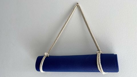 Eine blaue Yogamatte ist mit einem Seil aufgehängt, das sie sicher zusammenhält, vor einer hellen Wand.