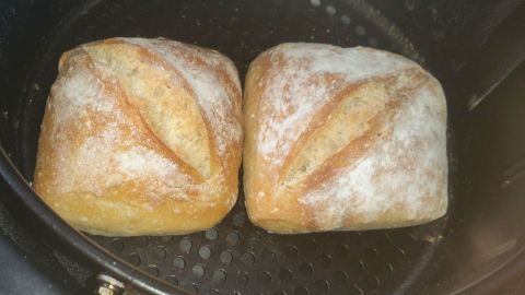 Zwei goldbraune Frühstücksbrötchen backen in einer Heißluftfritteuse, umgeben von der schwarzen Gitterstruktur des Geräts.