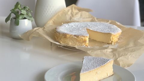 Ein leckerer Käsekuchen ohne Boden steht auf einem Tisch, umgeben von frischen Blumen und einem kleinen Pflanzenarrangement.