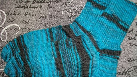 Bunte Stricksocken liegen auf einem grauen, beschrifteten Hintergrund und bieten Komfort gegen Hornhaut an den Füßen.