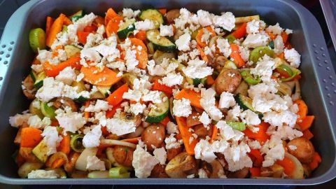 Bunte Mischung aus Ofengemüse wird mit zerbröckeltem Feta überhäuft und wartet in einer Auflaufform auf das Backen.