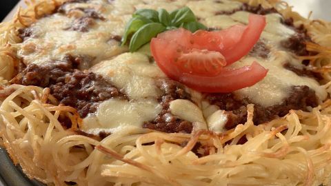 Eine appetitliche Spaghetti-Bolognese-Torte zeigt einen goldbraun gebackenen Nudelteig, garniert mit Käse, Tomate und Basilikum.