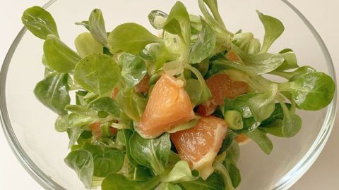 Frischer Feldsalat liegt in einer Glas-Schüssel, vermischt mit orangenen Stückchen, die appetitlich leuchten.